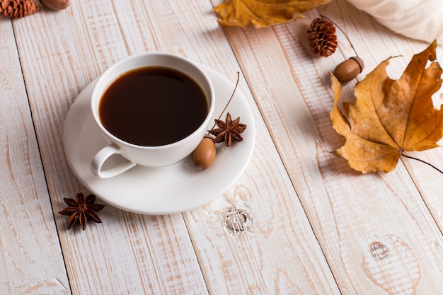 Sciarpa bianca, tazza di caffè e foglie gialle asciutte su una tavola di legno. Mood autunnale, copyspace.