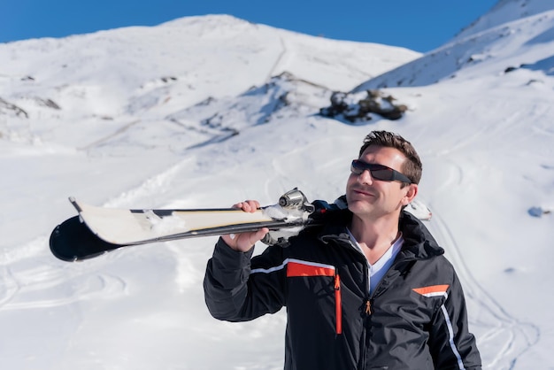 Sciatore con gli sci in spalla che guarda di lato e sorride in mezzo alla montagna innevata