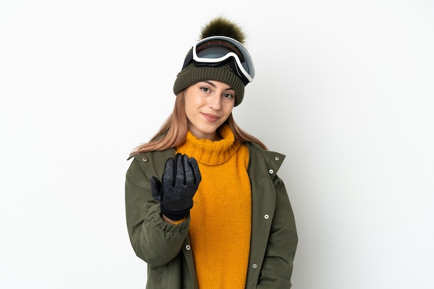 Sciatore donna caucasica con occhiali da snowboard isolati su bianco che invita a venire con la mano. Felice che tu sia venuto