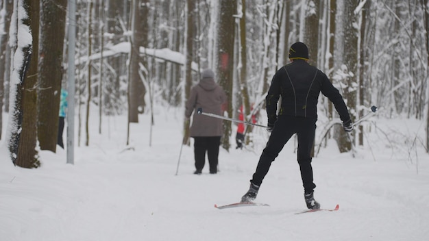 Sciatore uomo in giacca nera scivola nella foresta di neve invernale, teleobiettivo