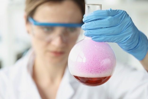 Scienziata che tiene in mano una boccetta con liquido viola con schiuma nei test chimici di laboratorio
