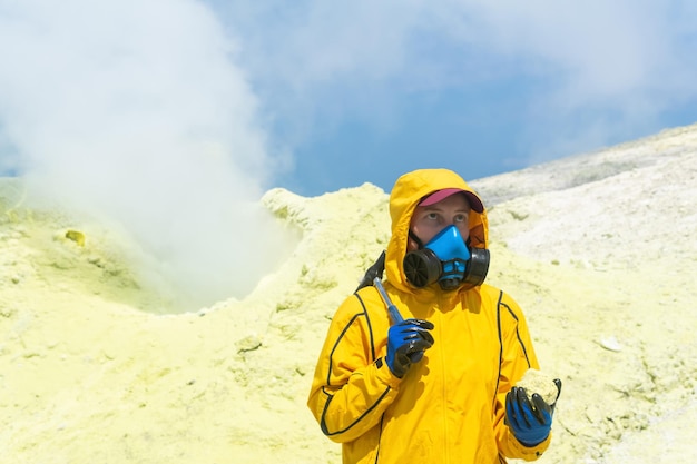 Scienziata del vulcano femminile con un martello geologico e un campione di un minerale sullo sfondo di una fumarola sul pendio di un vulcano