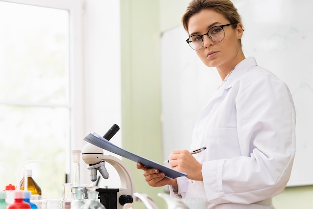 Scienziata della giovane donna che scrive un rapporto in un laboratorio durante il lavoro di ricerca