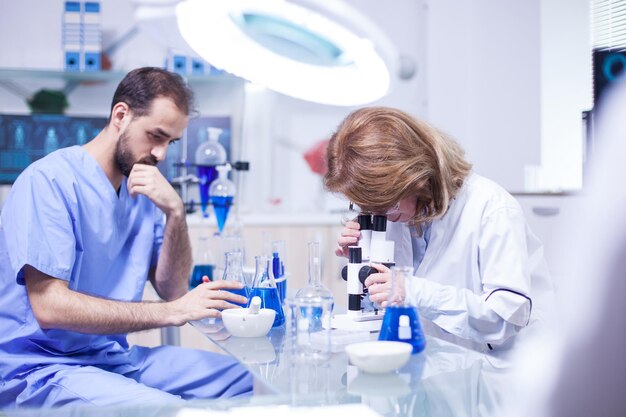 Scienziata di mezza età che lavora con il microscopio in laboratorio. Giovane maschio caucasico che lavora come tecnico in un laboratorio di ricerca.