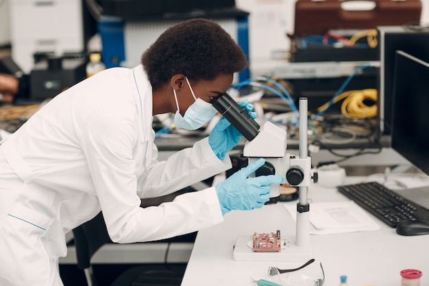 Scienziata donna afroamericana che lavora in laboratorio con strumenti tecnologici elettronici e ricerca al microscopio e sviluppo di dispositivi elettronici per colore donna nera