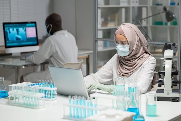 Scienziata musulmana in hijab e indumenti da lavoro protettivi digitando per posto di lavoro