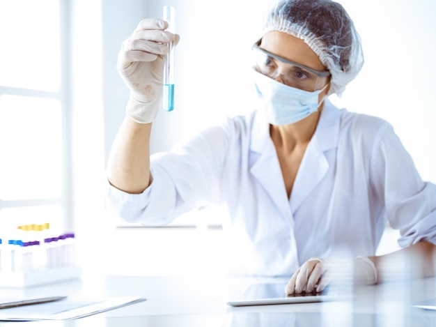 Scienziata professionista in occhiali protettivi che ricerca tubo con reagenti in laboratorio. Concetti di medicina e ricerca scientifica.