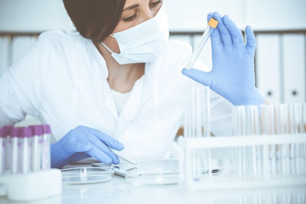 Scienziata professionista in occhiali protettivi e maschera che fa esperimenti con i reagenti in laboratorio. Stop alla pandemia di coronavirus. Concetto di medicina e ricerca.