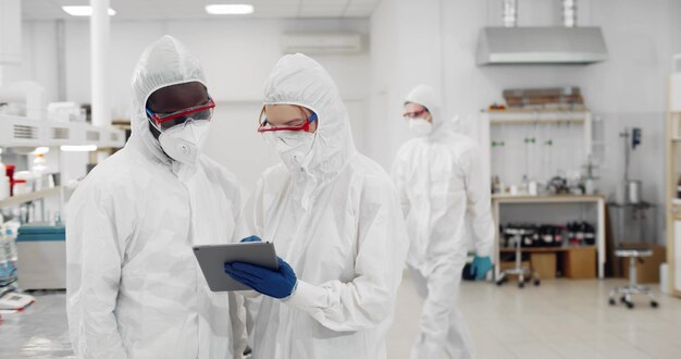 Scienziati in tuta che discutono dello sviluppo del vaccino guardando il tablet in un laboratorio attrezzato