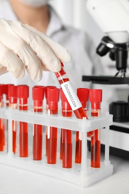Scienziato che preleva una provetta con campione di sangue ed etichetta CORONA VIRUS dal rack in primo piano del laboratorio