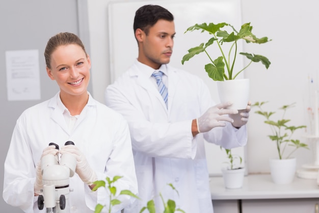 Scienziato che sorride alla macchina fotografica mentre collega che esamina pianta