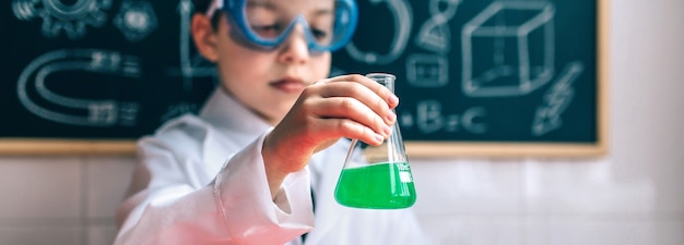 Scienziato del ragazzino con gli occhiali che tengono il pallone con liquido verde chimico contro la lavagna disegnata