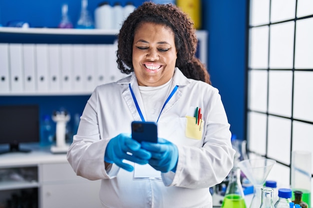 Scienziato donna afroamericana sorridente fiducioso utilizzando lo smartphone in laboratorio