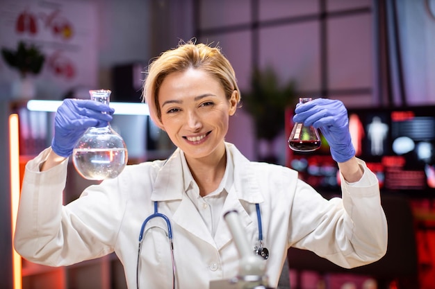 Scienziato femminile positivo o medico in camice da laboratorio che tiene la provetta con reagente