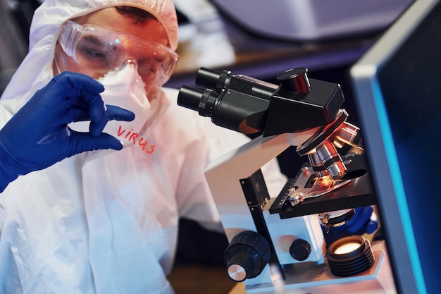 Scienziato in bianco protettivo indossare al chiuso in laboratorio con lente con il titolo di virus su di esso