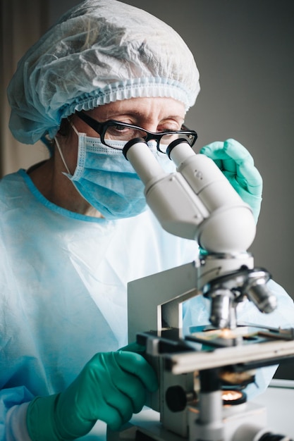 Scienziato in guanti medici blu e campioni di apprendimento uniforme con microscopio in laboratorio