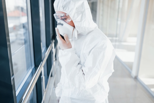 Scienziato medico femminile in camice da laboratorio, occhiali difensivi e maschera in piedi al chiuso