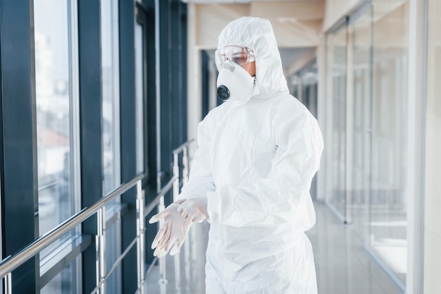 Scienziato medico femminile in camice da laboratorio, occhiali difensivi e maschera in piedi all'interno e indossando guanti