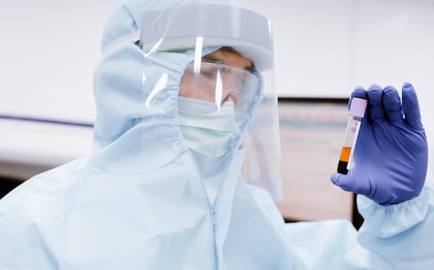 Scienziato medico in tenuta uniforme tuta DPI e guarda la provetta in laboratorio