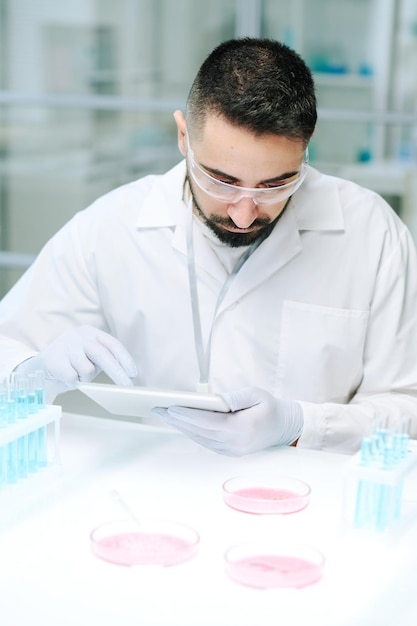 Scienziato o biotecnologo contemporaneo in camice bianco guanti e occhiali