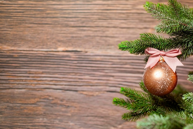 Scintillante pallina di Natale con fiocco rosa appeso al ramo di un albero di Natale su sfondo di legno con spazio copia, concetto di vacanza