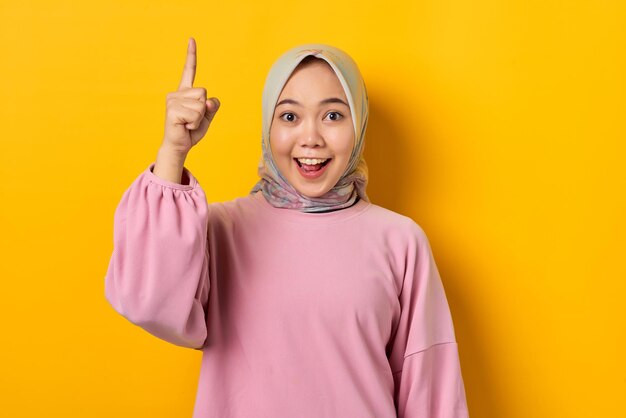 Scioccata giovane donna asiatica in camicia rosa che punta il dito verso l'alto avendo una buona idea su sfondo giallo