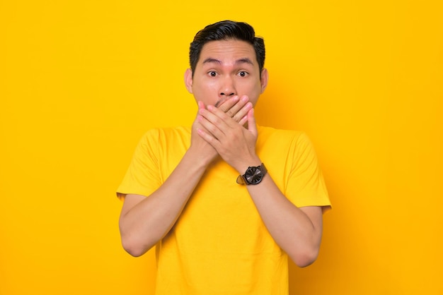 Scioccato giovane asiatico in maglietta casual che copre la bocca con le mani e guarda la fotocamera isolata su sfondo giallo Concetto di stile di vita delle persone