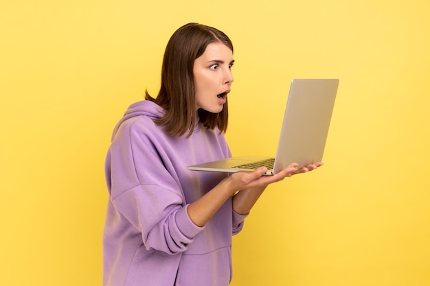 Scioccato giovane donna adulta che lavora al computer portatile guardando il display con la bocca aperta