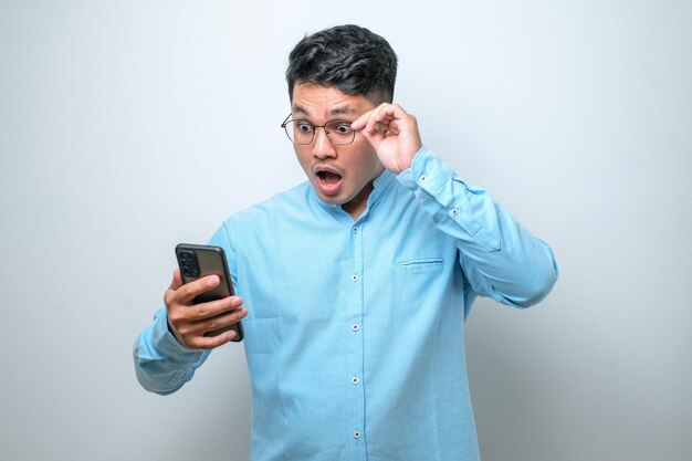 Scioccato giovane uomo asiatico di bell'aspetto che utilizza lo smartphone per leggere buone notizie online isolato