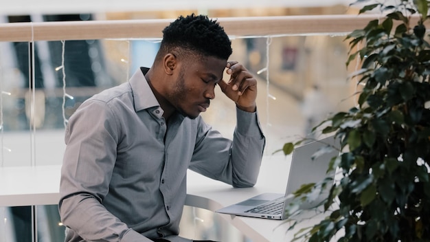 Scioccato giovane uomo d'affari che lavora al computer portatile sentendosi frustrato stressato dalla disperazione del problema