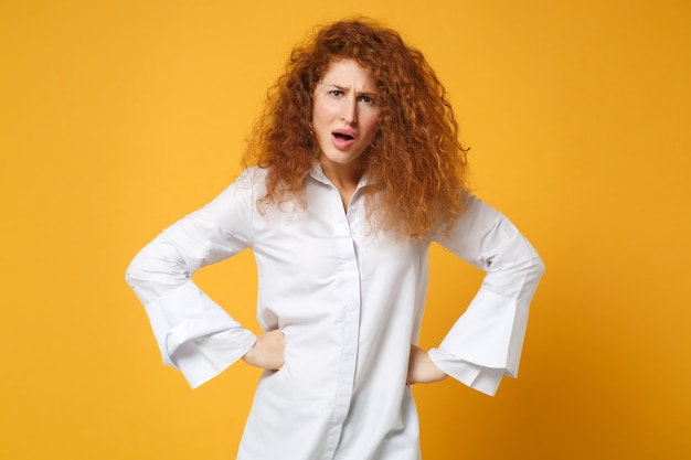 Scioccato irritato giovane donna rossa ragazza in camicia bianca casual in posa isolata sul muro giallo arancione