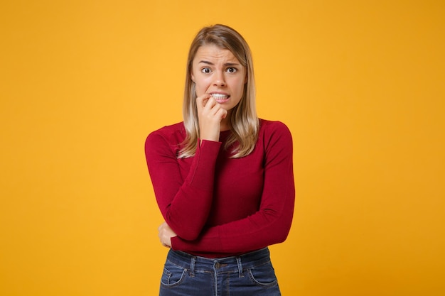 Scioccato perplesso giovane donna bionda ragazza in abiti casual in posa isolata sul ritratto in studio di sfondo muro giallo arancio. Concetto di stile di vita delle persone. Simula lo spazio della copia. Unghie rosicchiate, guardando da parte.