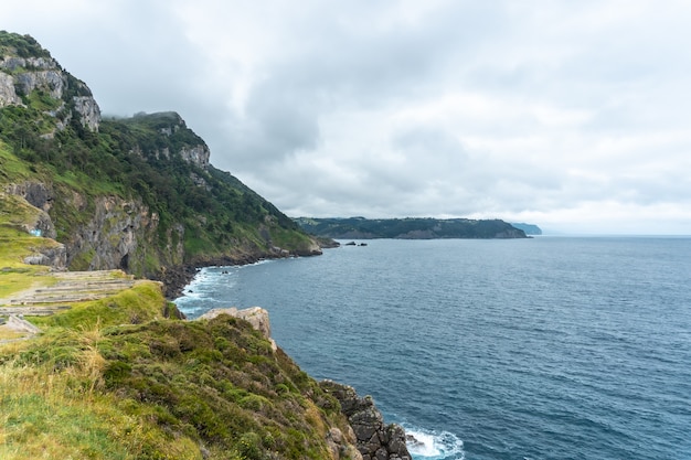 Scogliere accanto al faro di Santa Catalina de Lekeitio in una nuvolosa mattina di primavera, con il mare sullo sfondo, paesaggi di Bizkaia