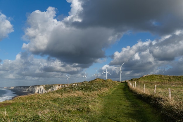 Scogliere in riva al mare sulla spiaggia di Ã‰tretat che si estende fino all'orizzonte con mulini a vento elettrici sullo sfondo del cielo drammatico