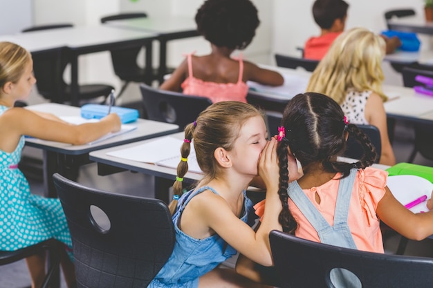 Scolara che bisbiglia nell'orecchio della sua amica in aula