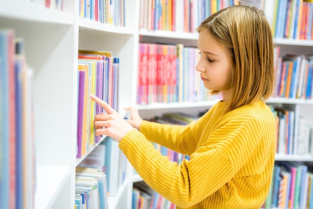 Scolara che sceglie il libro nella biblioteca della scuola