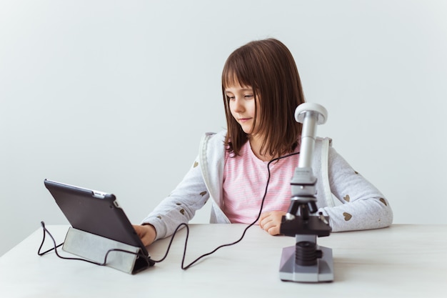 Scolara che utilizza microscopio nella classe di scienza. Tecnologie, lezioni e concetto di bambini.