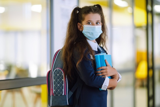 Scolara in una maschera protettiva con uno zaino e un libro di testo