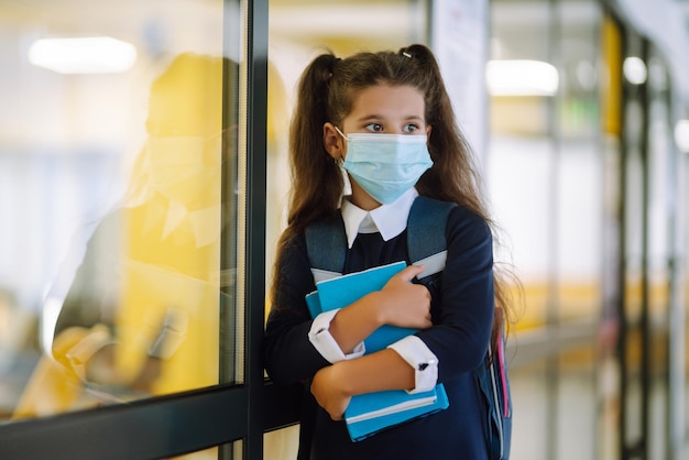 Scolara in una maschera protettiva con uno zaino e un libro di testo