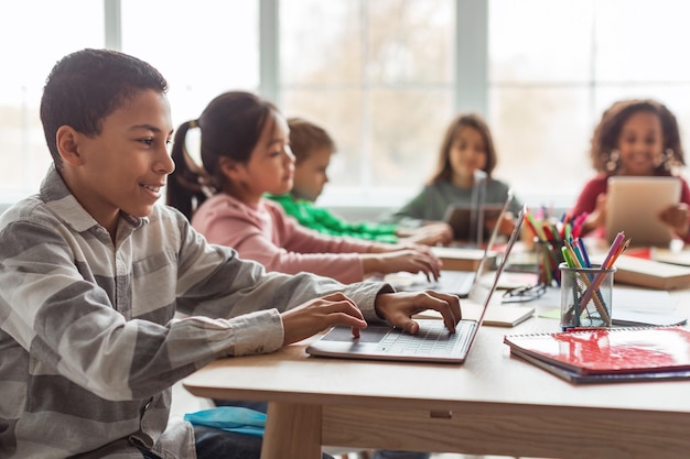 Scolaro afroamericano che utilizza il computer portatile che impara in linea a scuola