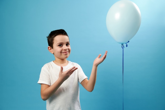 Scolaro bello che indica sul palloncino blu e sorrisi svegli che esaminano davanti