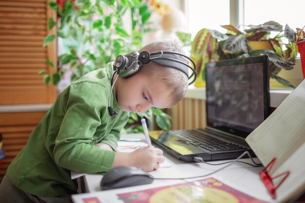 Scolaro carino di educazione a distanza che studia i compiti durante la lezione online a distanza sociale a casa