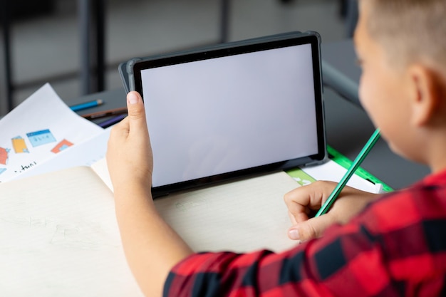 Scolaro caucasico seduto alla scrivania usando il tablet in classe copia lo spazio sullo schermo