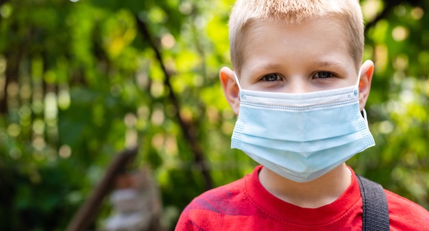 Scolaro che indossa una maschera facciale durante l'epidemia. Ritorno al concetto di scuola. Ragazzo carino fuori a scuola che si diverte. Maschera di sicurezza per la prevenzione del coronavirus. Bambino con lo zaino che va a scuola. Formazione scolastica.