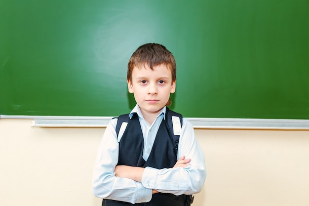 Scolaro divertente vicino al consiglio scolastico verde in classe. Bambino della scuola elementare. Di nuovo a scuola.