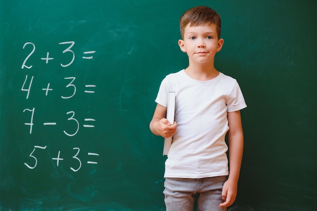 Scolaro divertente vicino al consiglio scolastico verde in classe. Scuola elementare. Di nuovo a scuola.