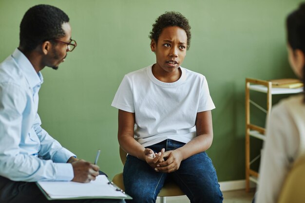 Scolaro infelice di Preteen che descrive il suo problema al compagno di classe mentre si siede davanti all'amer africano