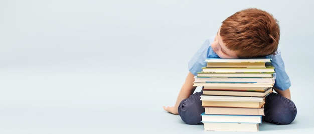 Scolaro sconvolto seduto con una pila di libri di scuola Ragazzo che dorme su una pila di banner di libri di testo