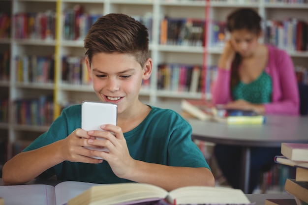 Scolaro sorridente che utilizza telefono cellulare nella biblioteca