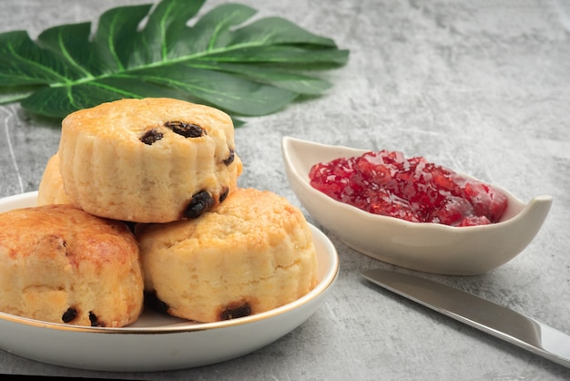 Scone in piatto bianco e marmellata di fragole su fondo di cemento